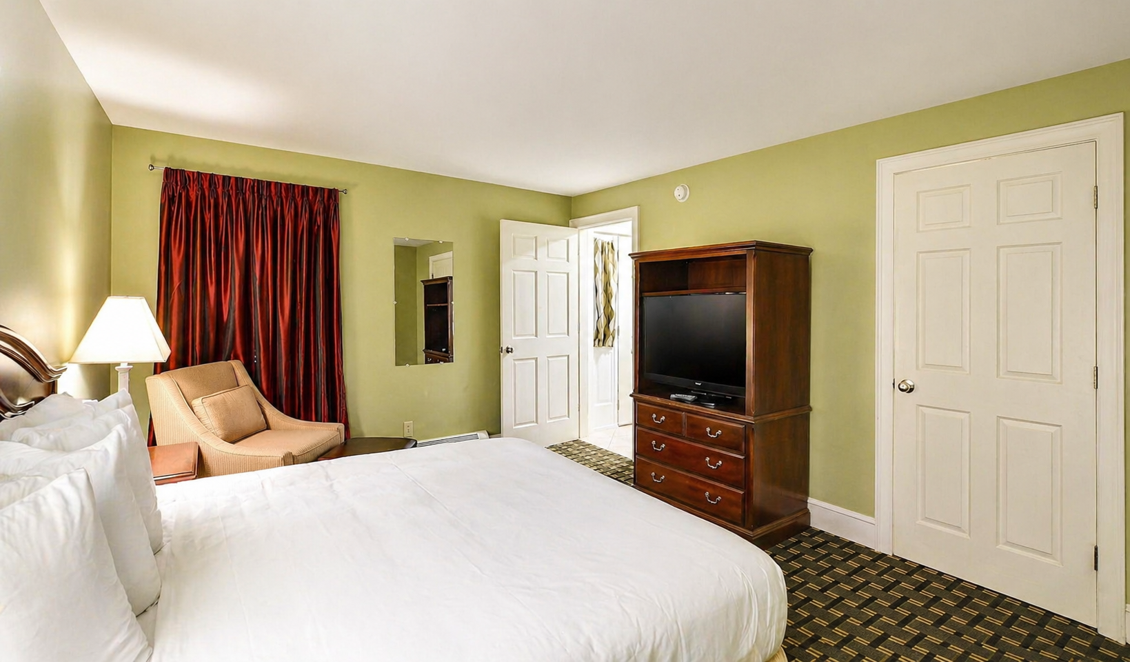 Bedroom with a white bed, green walls, red curtains, dresser, and TV near a window and closet doors