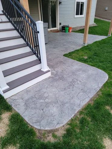 Staircase leading down to a patterned concrete patio with grass surrounding it.