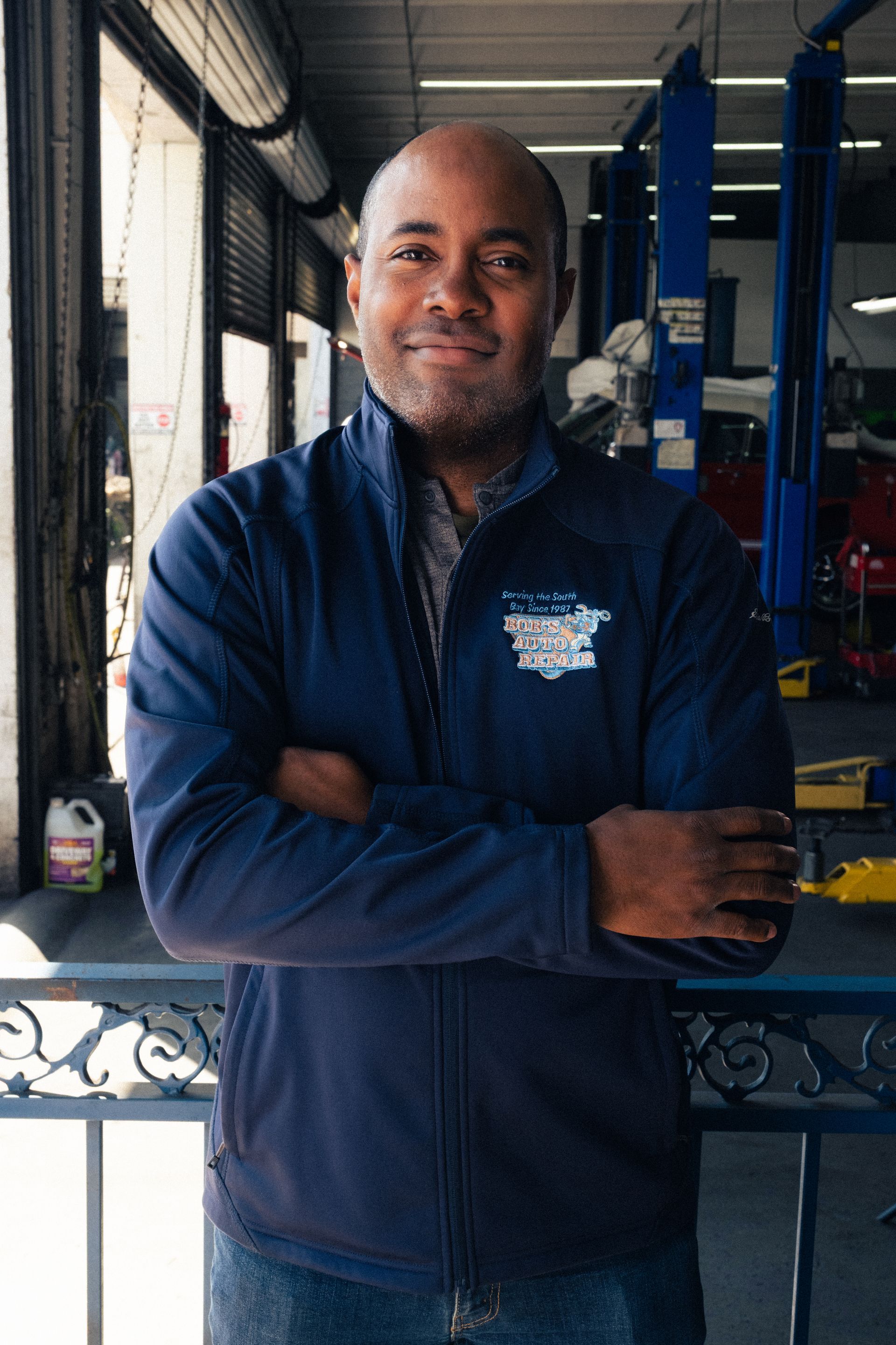 Man standing with arms crossed in a blue jacket inside an industrial workshop