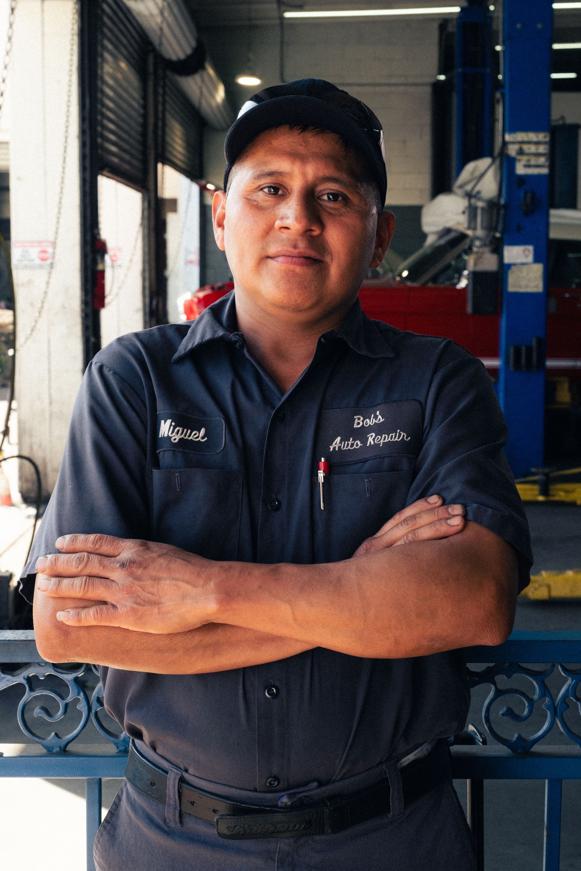 Man in navy work shirt and cap standing with arms crossed in a garage workspace