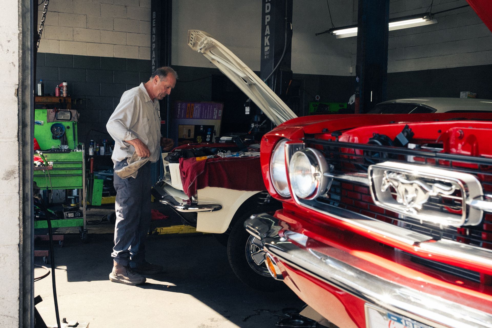 Mechanic working on a red classic car in a garage with the hood open