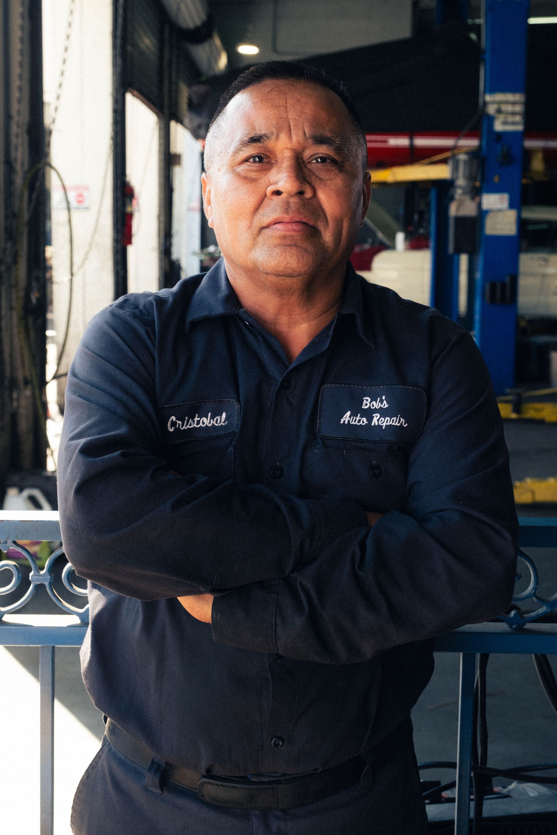 Mechanic in navy coveralls stands with arms crossed in a garage workshop.
