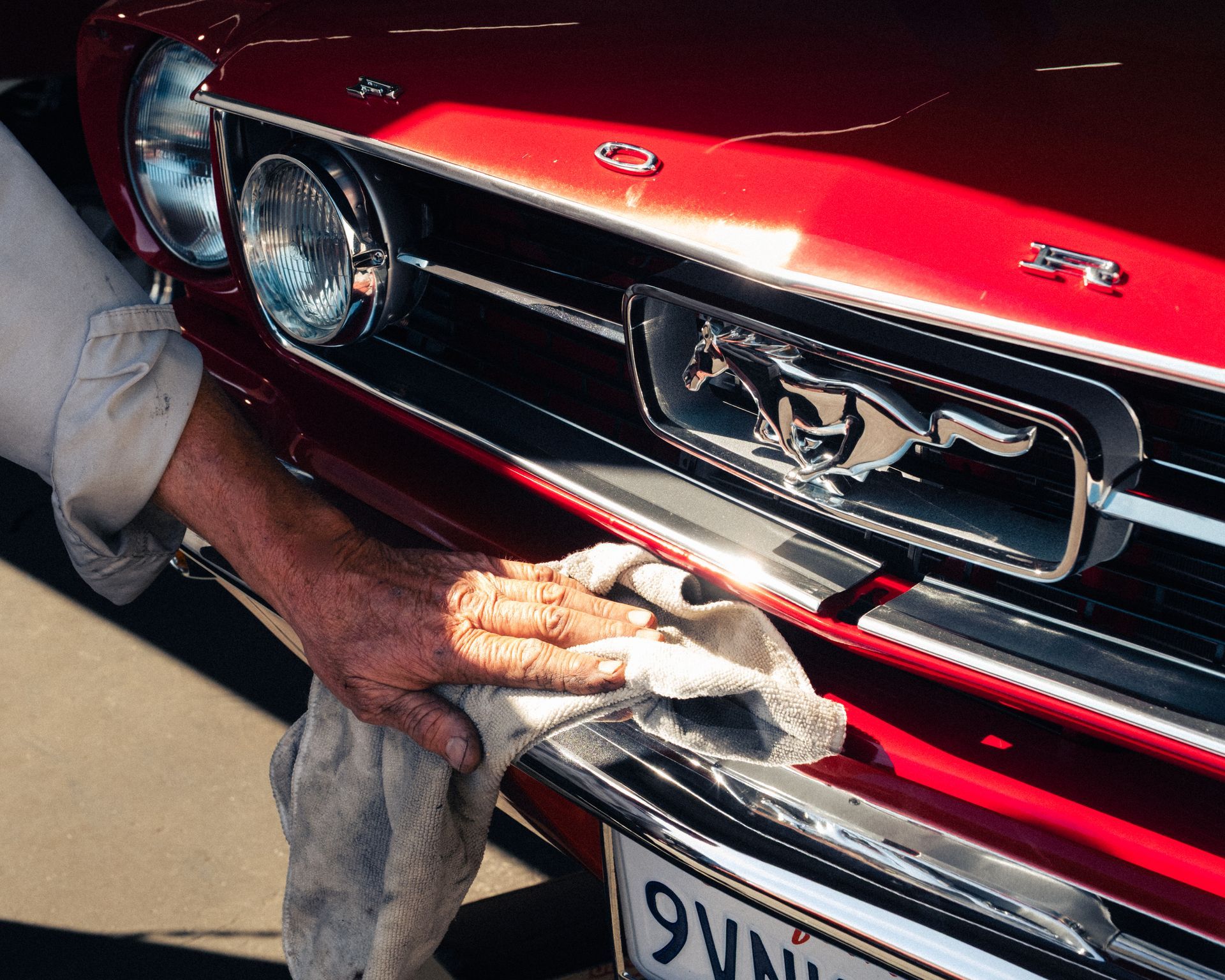 Hand wiping the front grille of a red Ford Mustang with a cloth