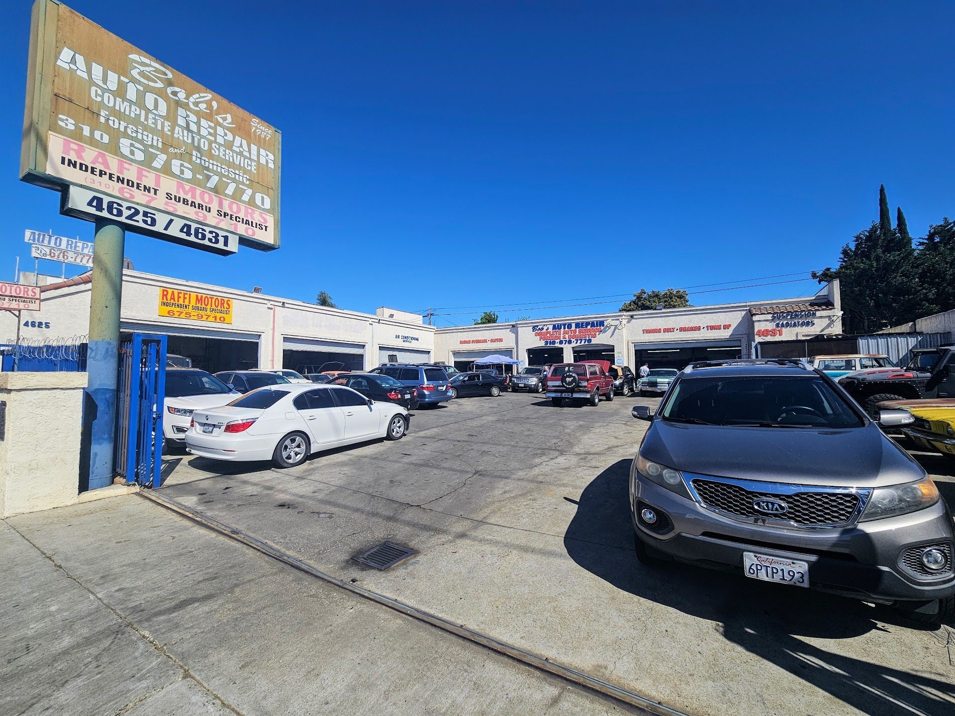 Auto repair shop with parked cars under a blue sky. Sign reads 