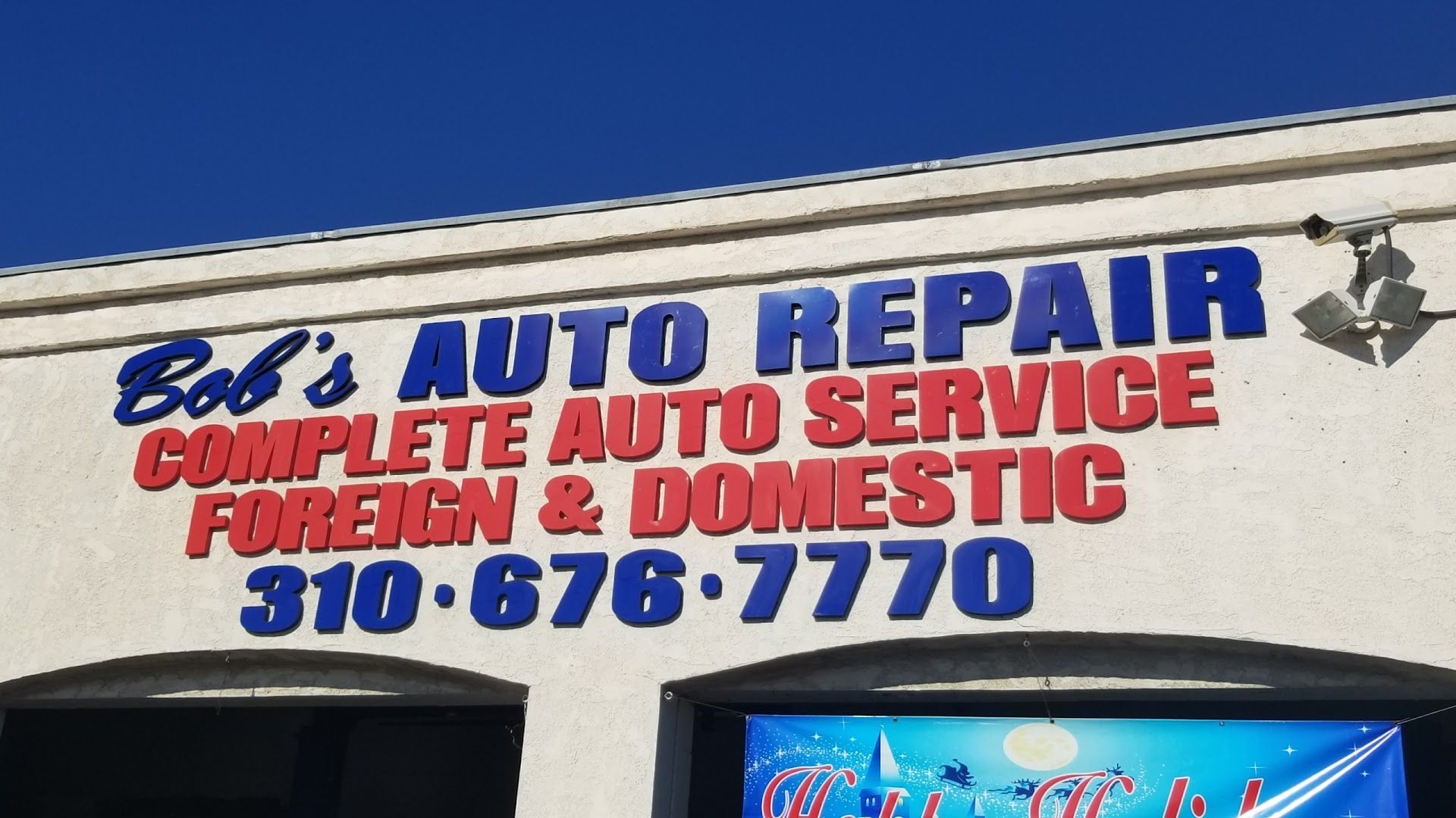 Sign for Bob's Auto Repair, listing services and phone number, with blue lettering on a white building against a blue sky | Bob's Auto Repair