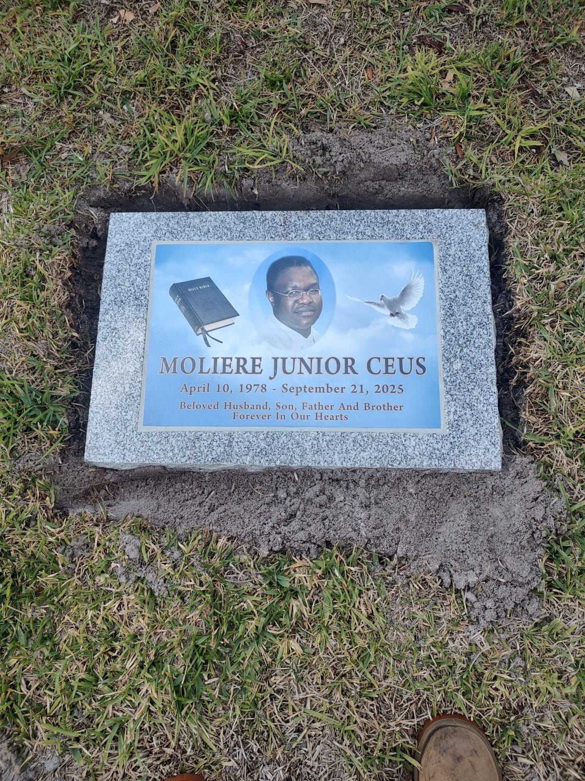 Headstone with portrait, dove, and open book, set in grass. Reads 