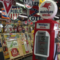 A red Mobilgas gas pump stands in a shop filled with vintage oil company signs and advertisements.