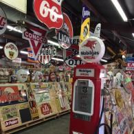 A vintage red Mobilgas gas pump surrounded by various colorful antique gasoline and advertising signs in a warehouse.