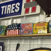 A row of vintage metal lunchboxes on a store shelf, including an American flag design and a yellow Snoopy lunchbox.