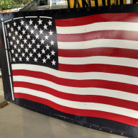 A stylized, waving American flag painted on a metal surface with visible rivets and a black border.