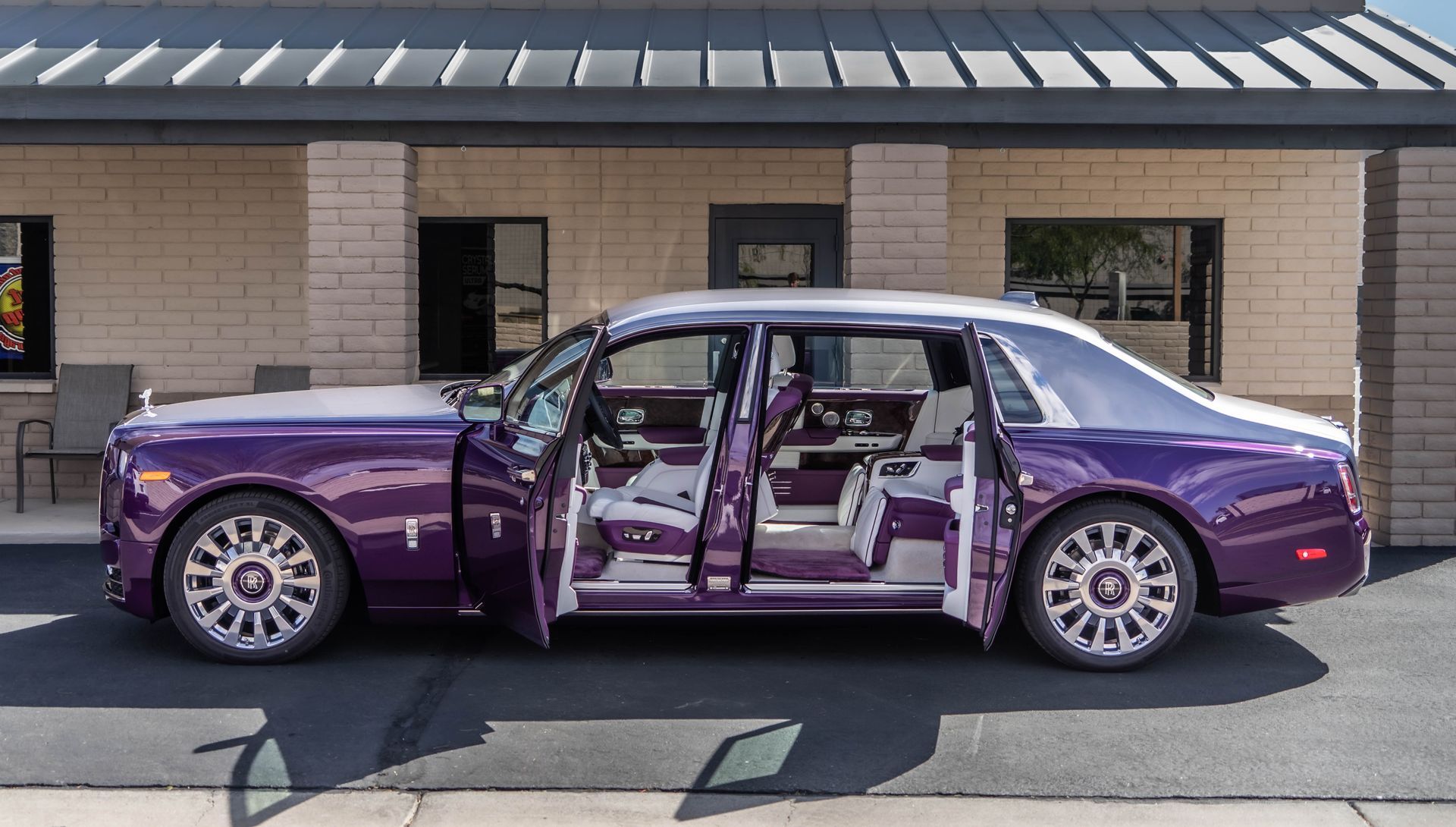 A purple car is parked in front of a building with its doors open.