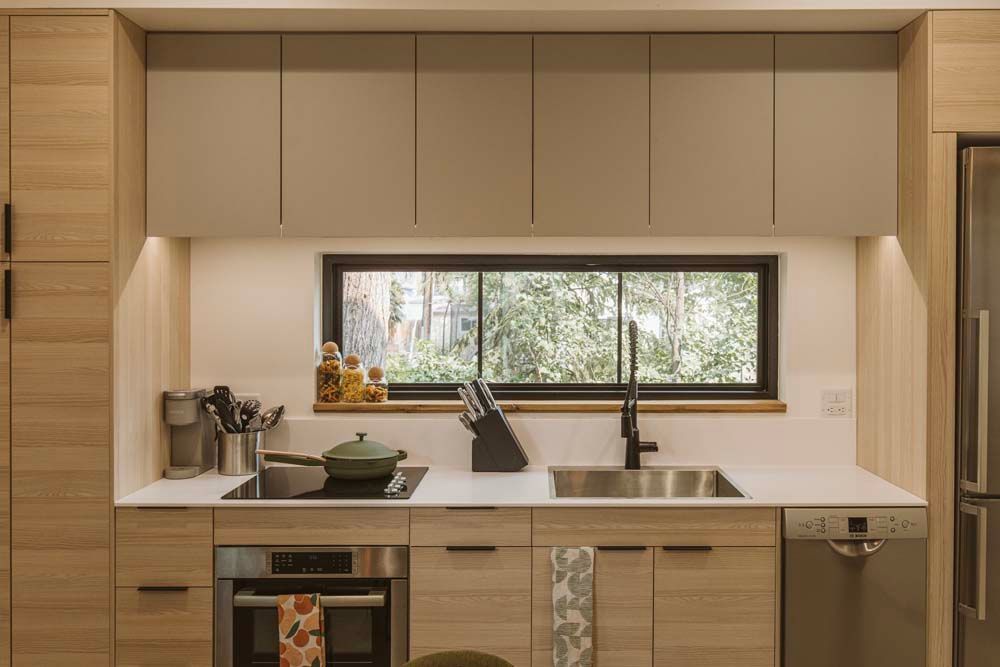 A kitchen with stainless steel appliances , wooden cabinets , a sink , and a window.