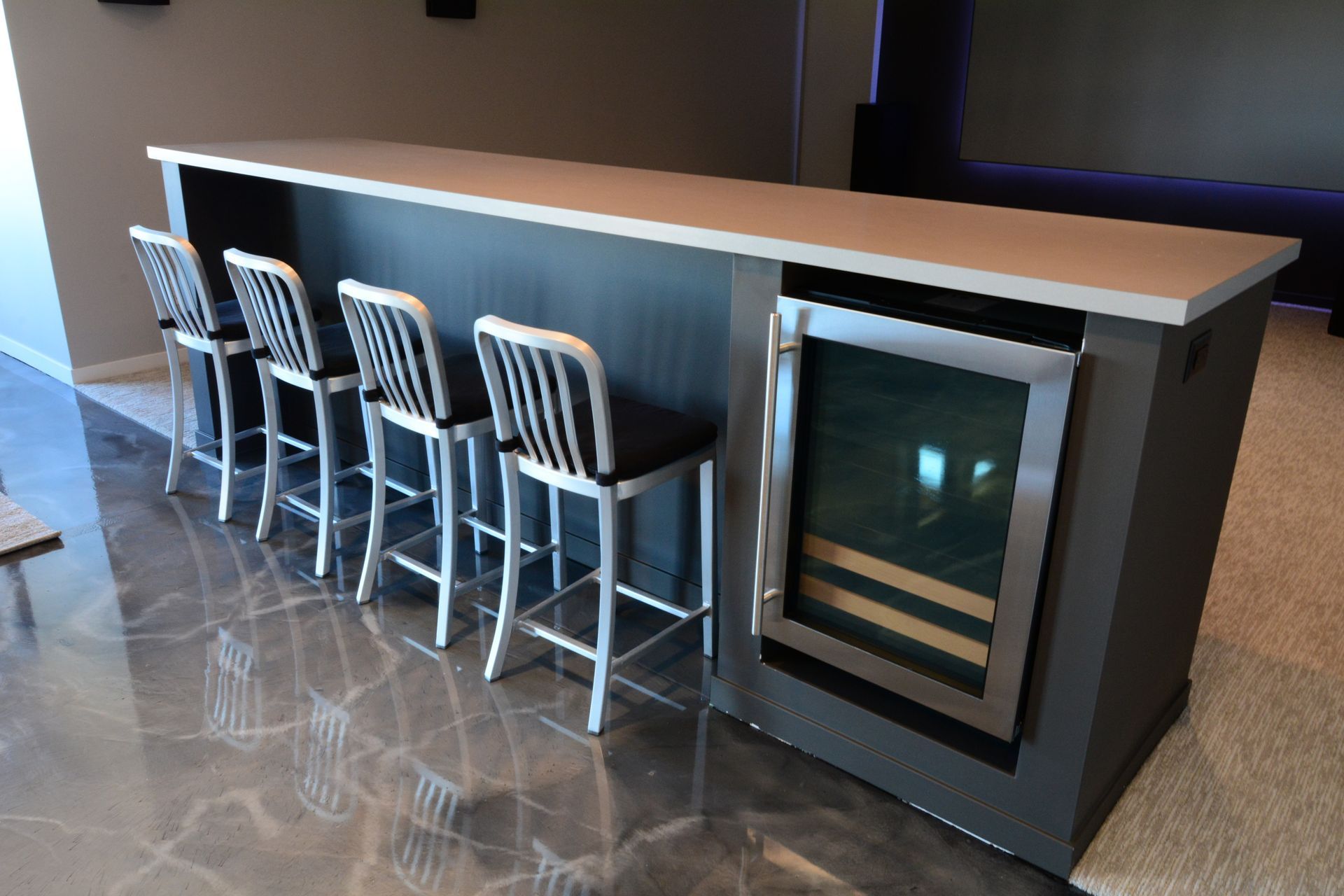 A bar with stools and a wine cooler underneath it