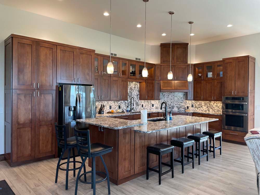 A kitchen with wooden cabinets , granite counter tops , stools and a large island.