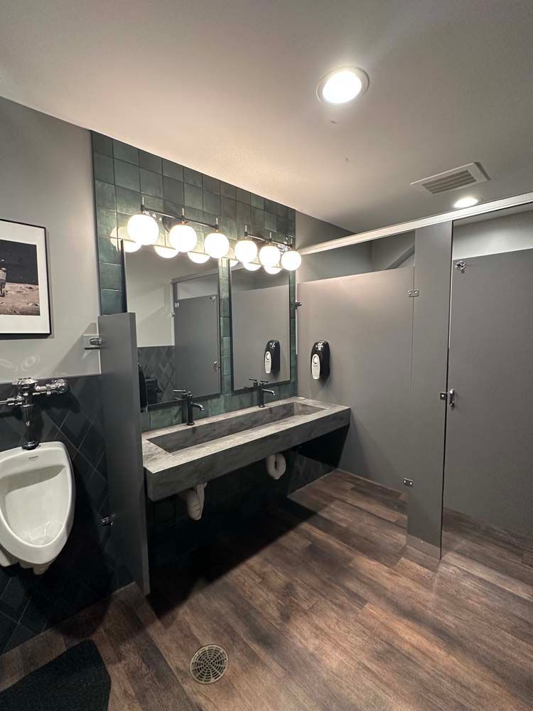 A public restroom with a sink , mirrors , and wooden floors.