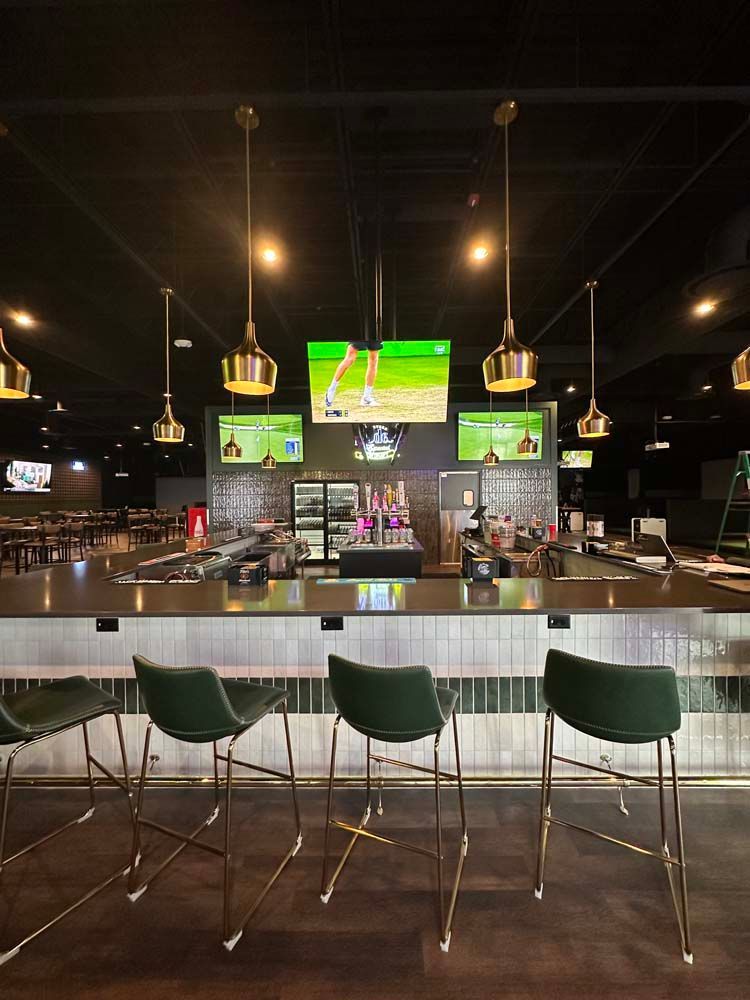 A bar with a lot of chairs and televisions on the wall.