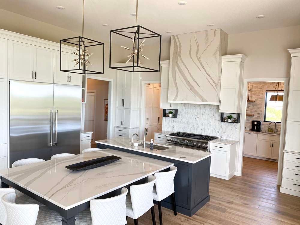 A kitchen with white cabinets , stainless steel appliances , a large island , a table and chairs.