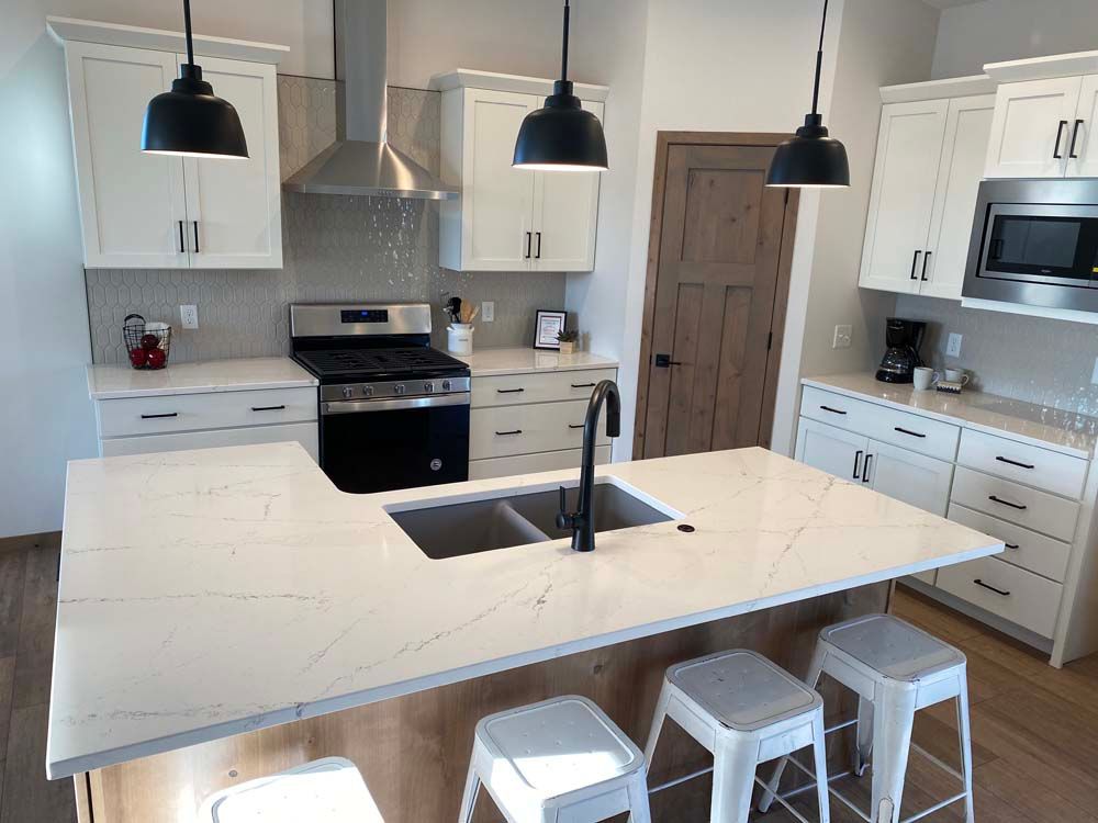 A kitchen with white cabinets , stainless steel appliances , a sink , and a large island.