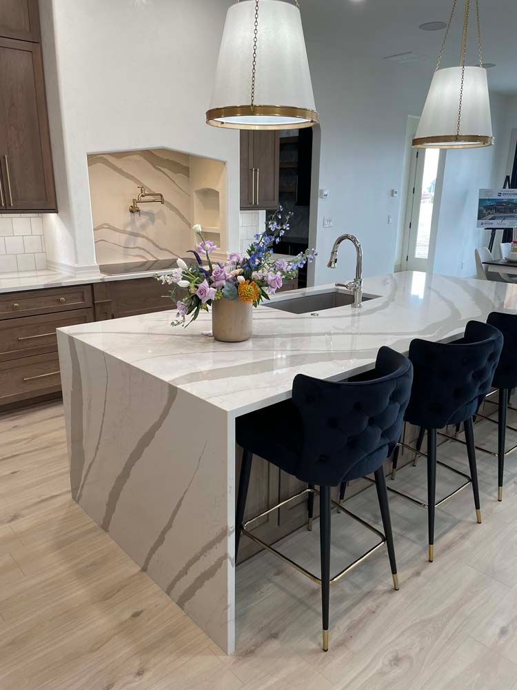 There is a large island in the middle of the kitchen with a vase of flowers on it.