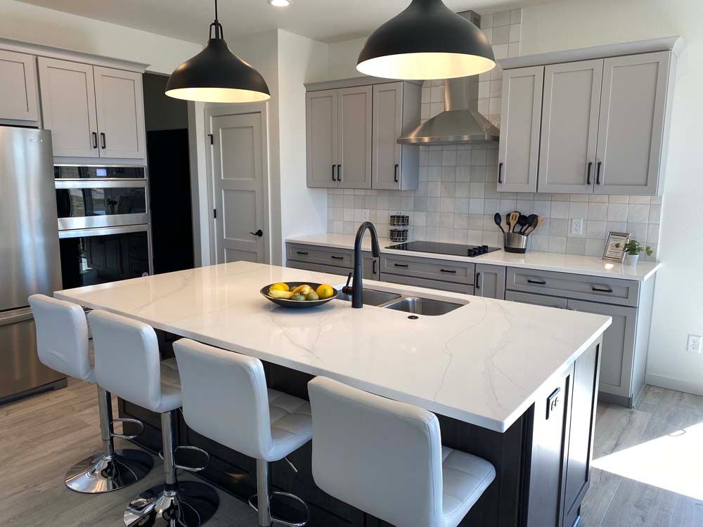 A kitchen with gray cabinets , white counter tops , stainless steel appliances and a large island.