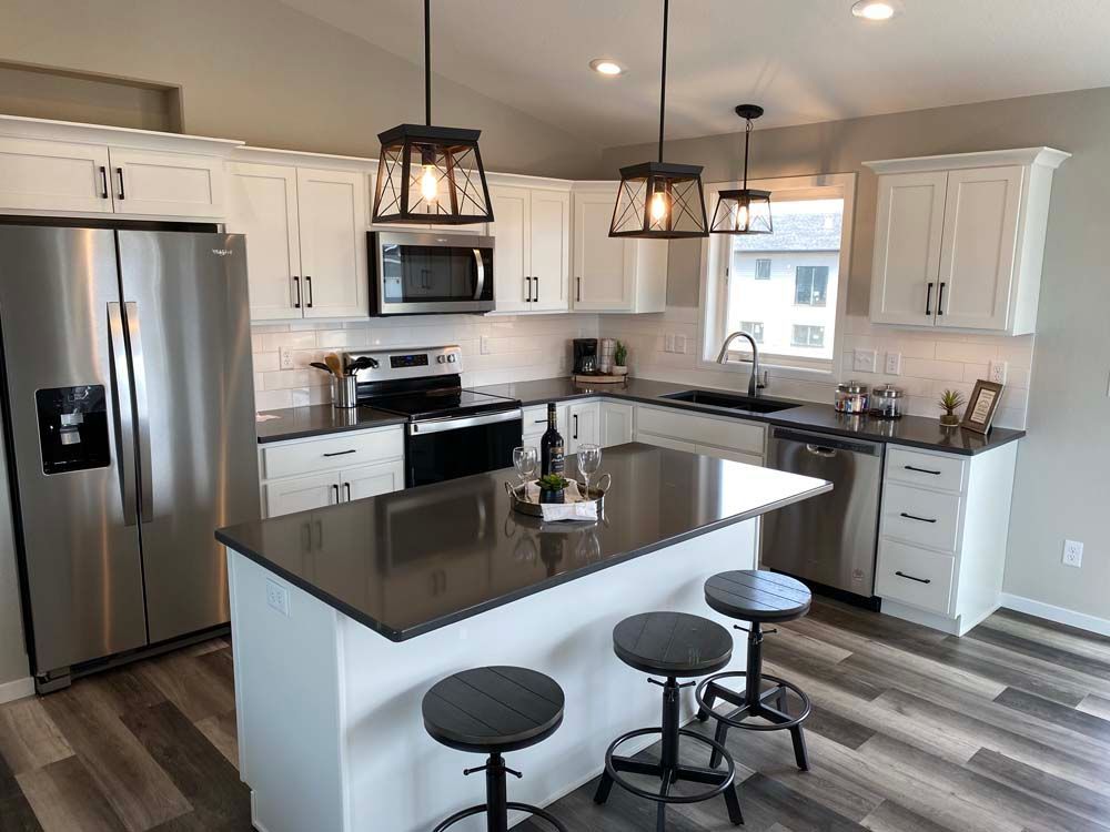 A kitchen with white cabinets , stainless steel appliances , granite counter tops and a large island.