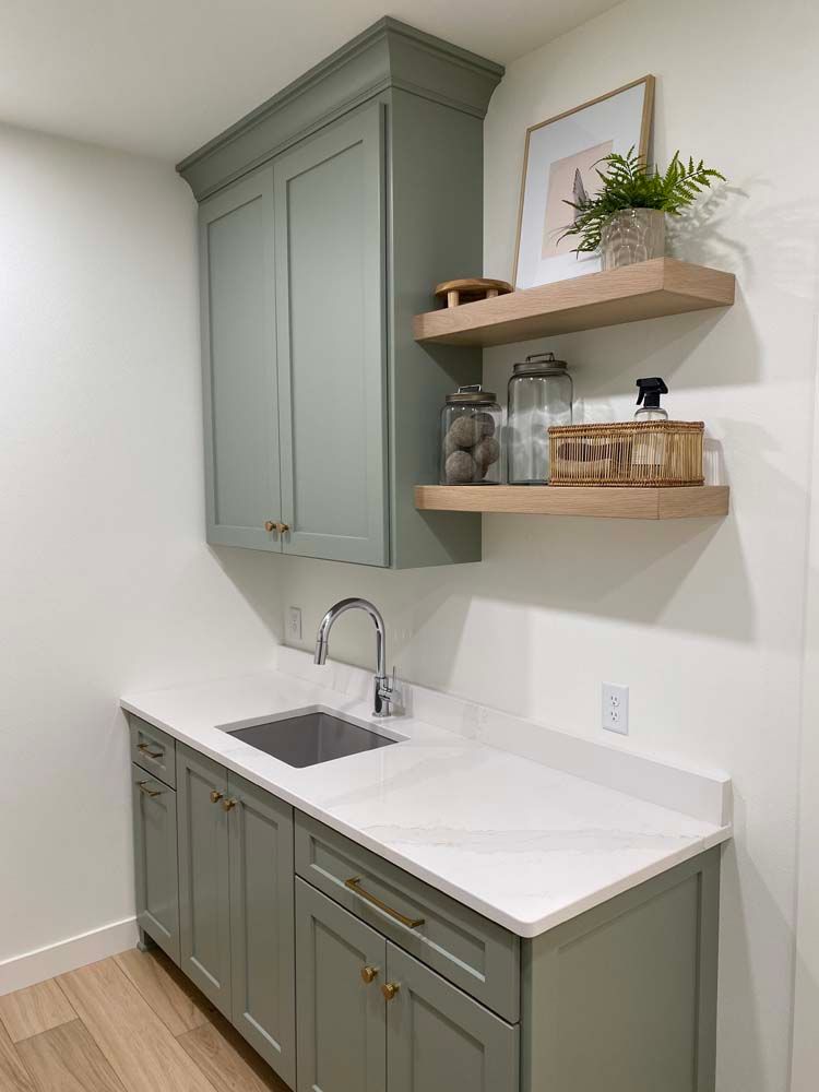 A laundry room with a sink , cabinets , and shelves.