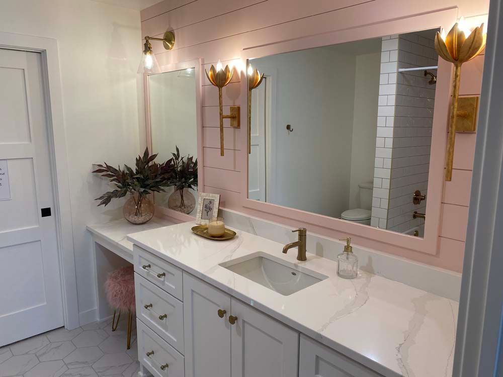 A bathroom with a pink wall , white cabinets , a sink and a large mirror.