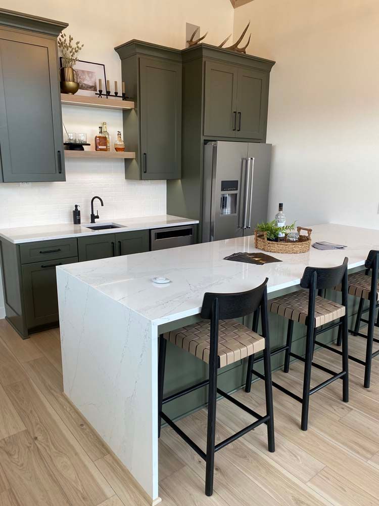 A kitchen with a large island , stools and a refrigerator.