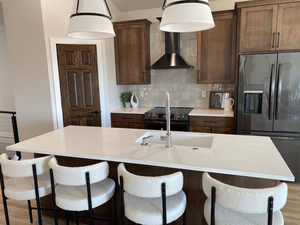 A kitchen with a large island , sink , refrigerator , stove and chairs.