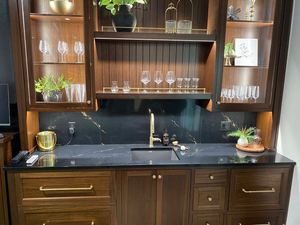 A kitchen with a sink , cabinets , shelves and glasses.