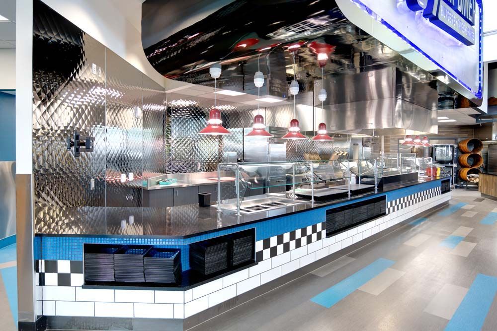 A long buffet line in a restaurant with blue and white tiles and stainless steel appliances.