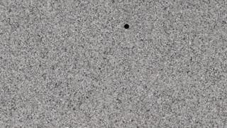 A close up of a gray carpet with a black hole in the middle.
