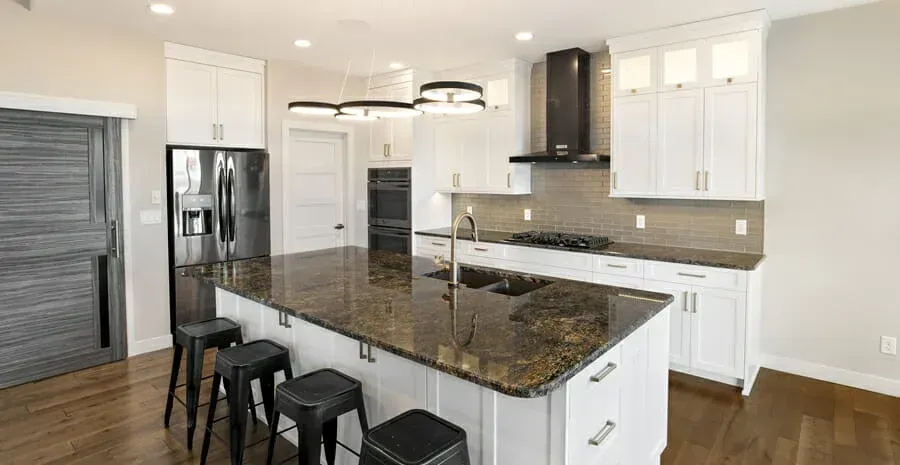 A kitchen with white cabinets , granite counter tops , stools and a large island.