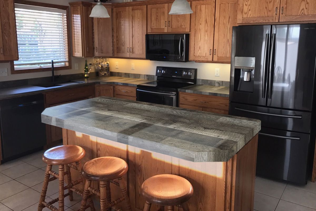 A kitchen with a large island , stools , a refrigerator and a stove.