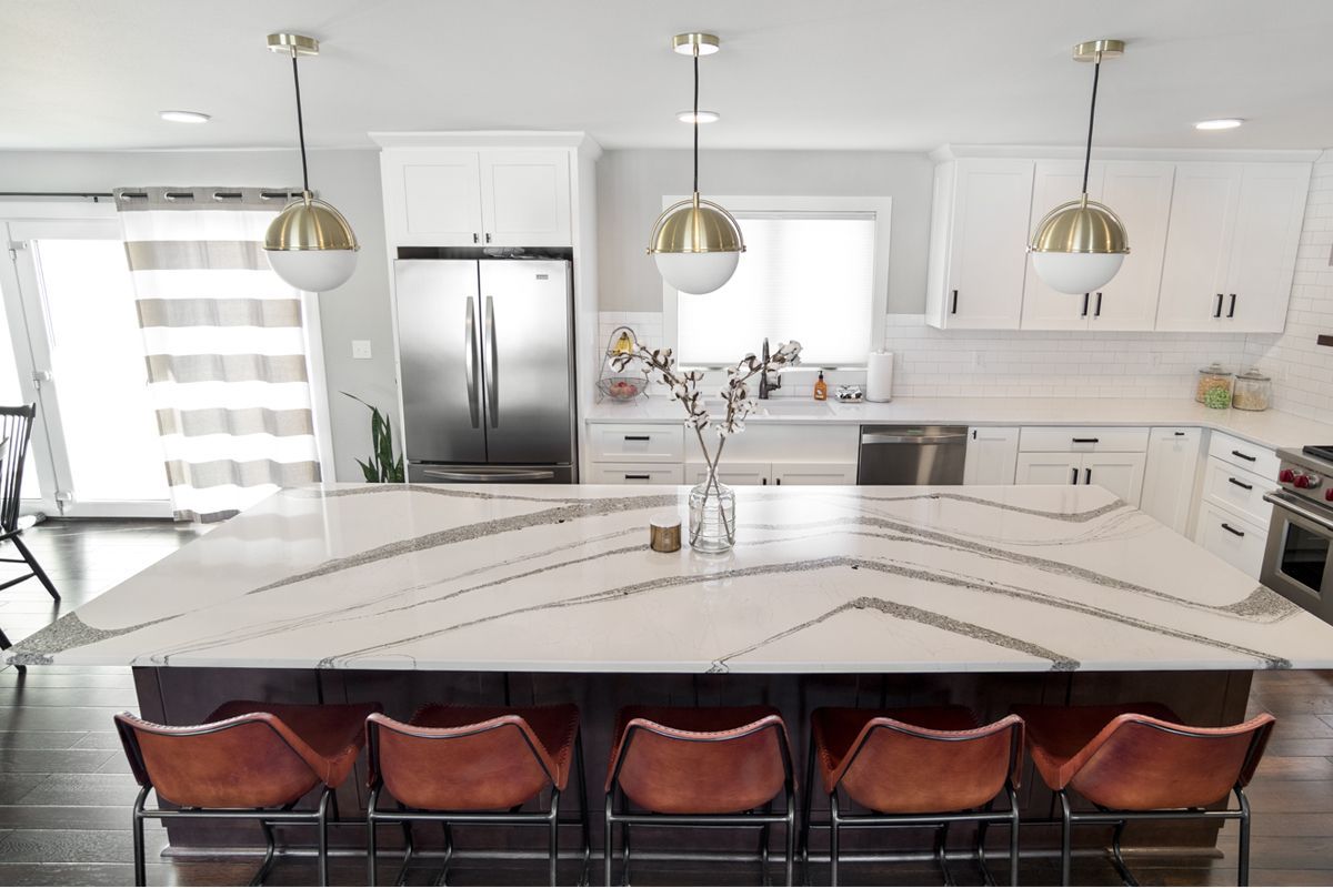 A kitchen with a large island , stools and a refrigerator.