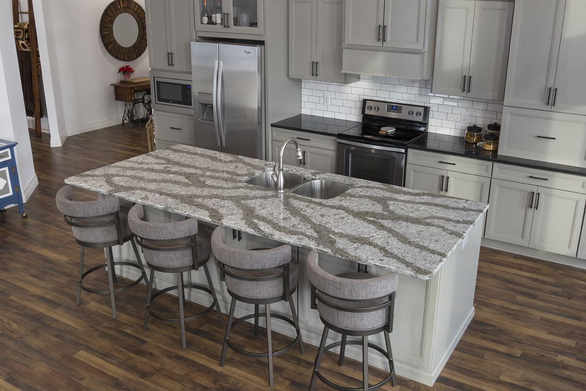 A kitchen with a large island , stools , a sink and a refrigerator.