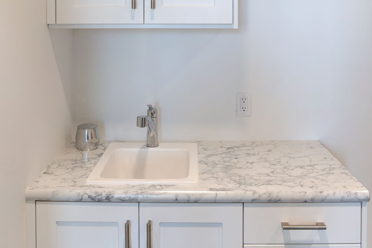 A laundry room with a sink , cabinets , and granite counter tops.