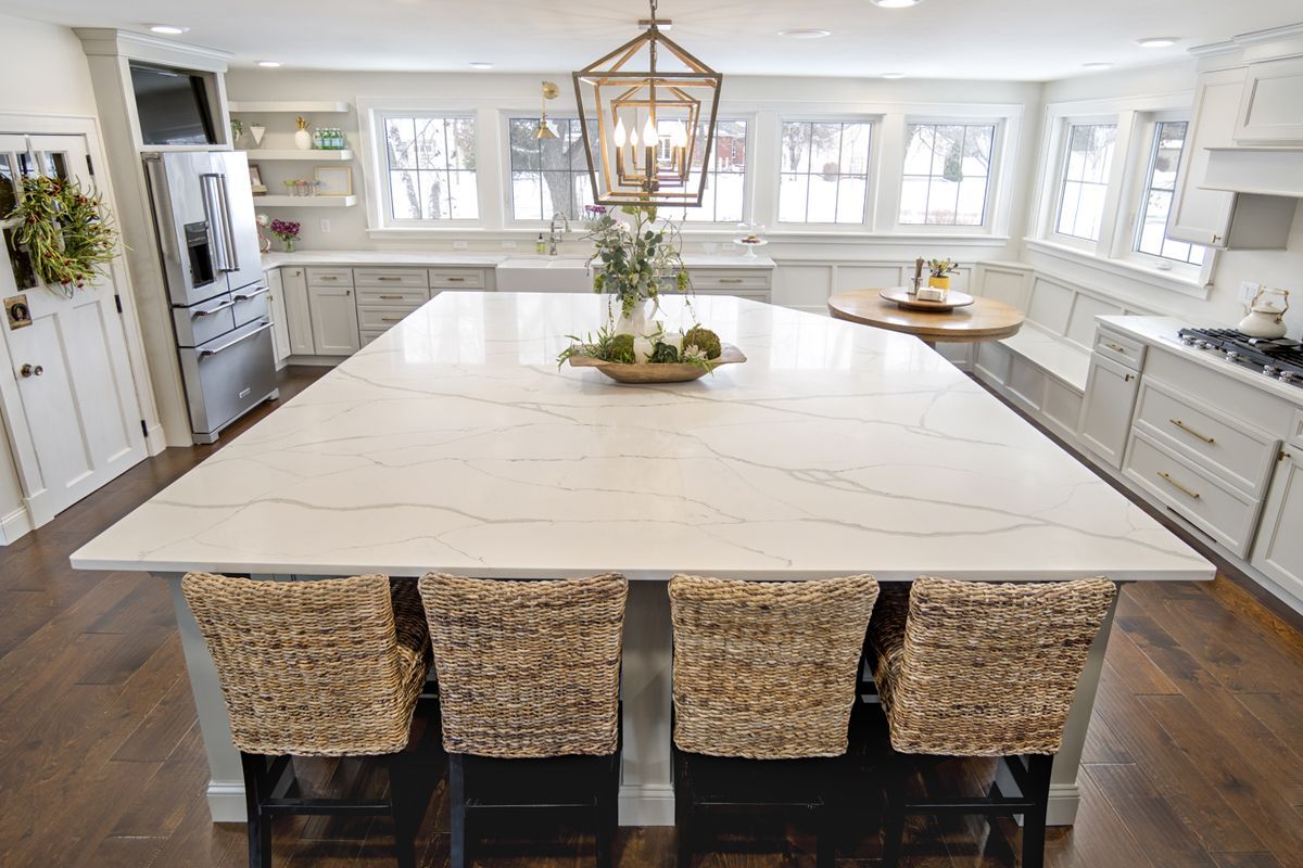 A kitchen with a large island and wicker chairs.