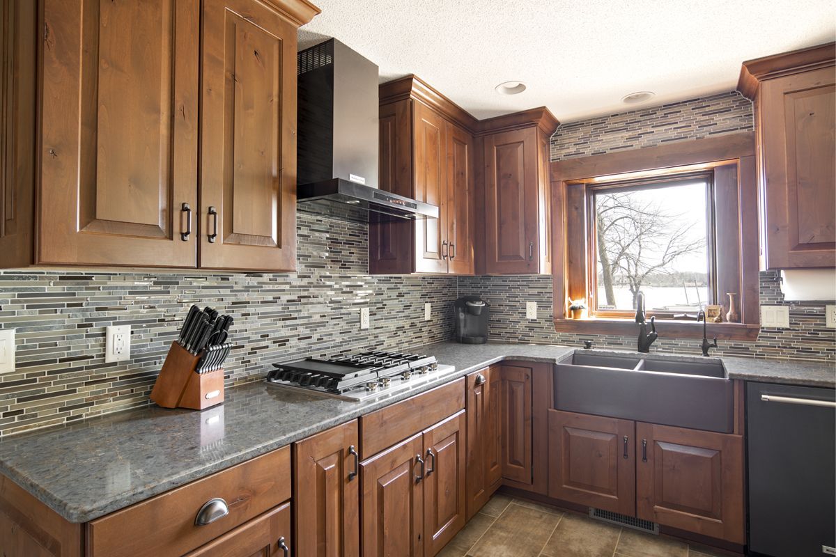 A kitchen with wooden cabinets , granite counter tops , a stove and a sink.