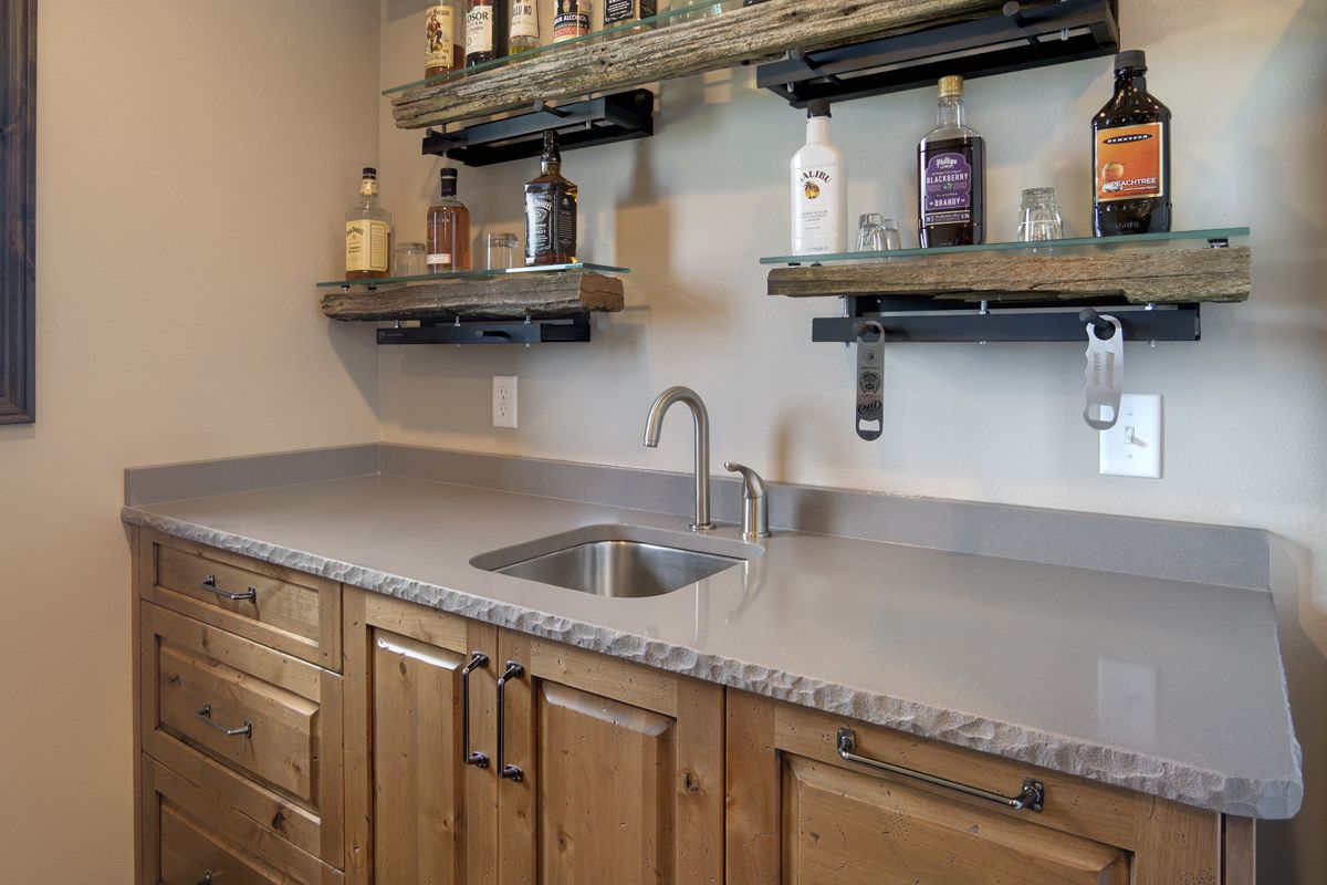 A kitchen with a sink and shelves filled with bottles of alcohol.