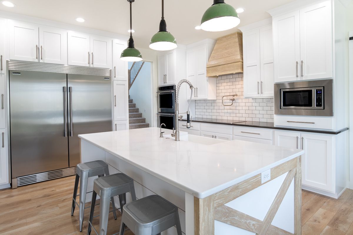 A kitchen with white cabinets , stainless steel appliances , and a large island.