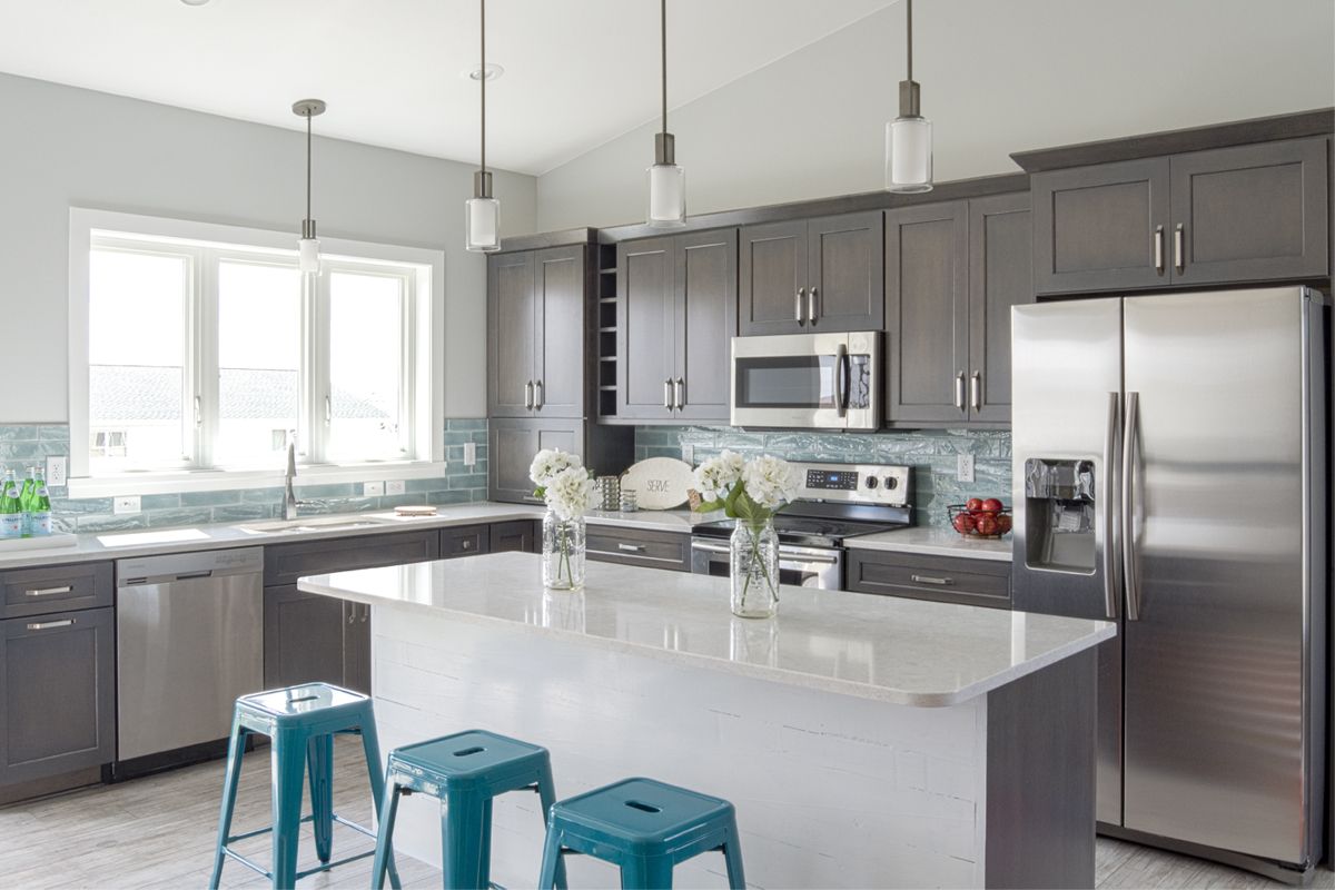 A kitchen with gray cabinets , stainless steel appliances , a large island , and blue stools.