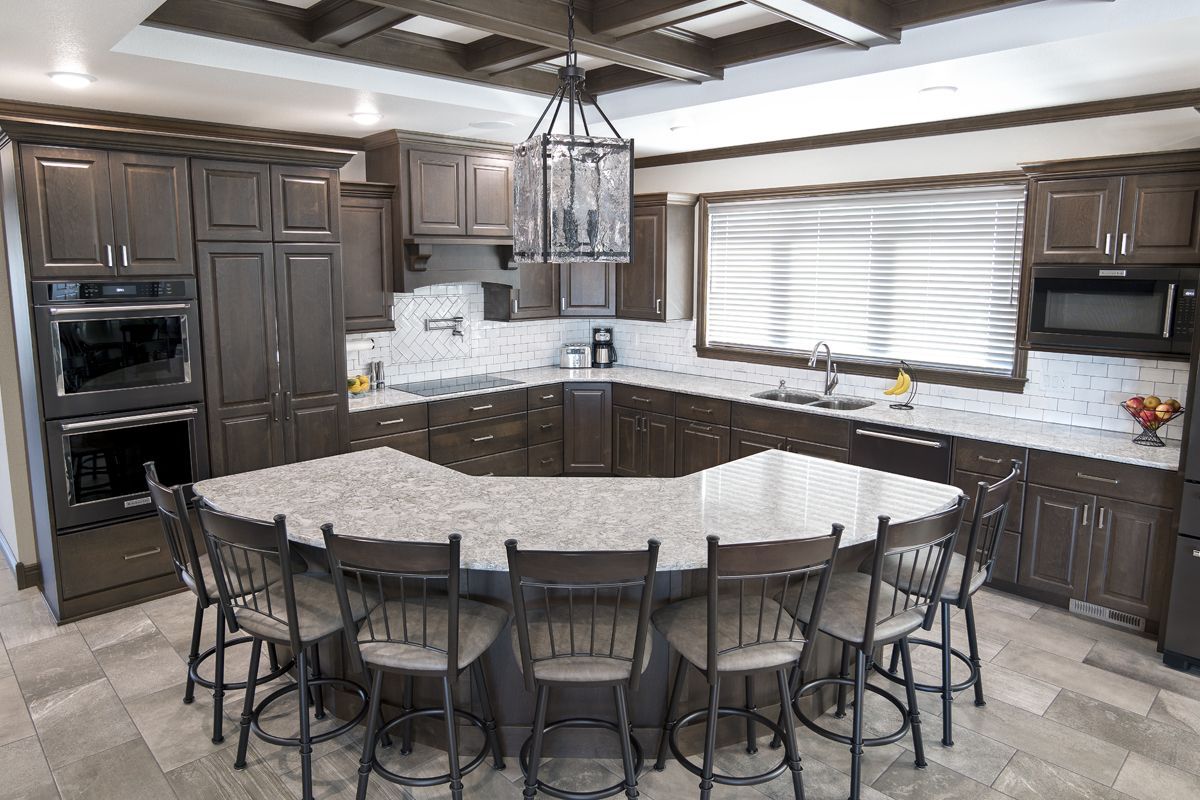 A kitchen with a large island in the middle and chairs around it.