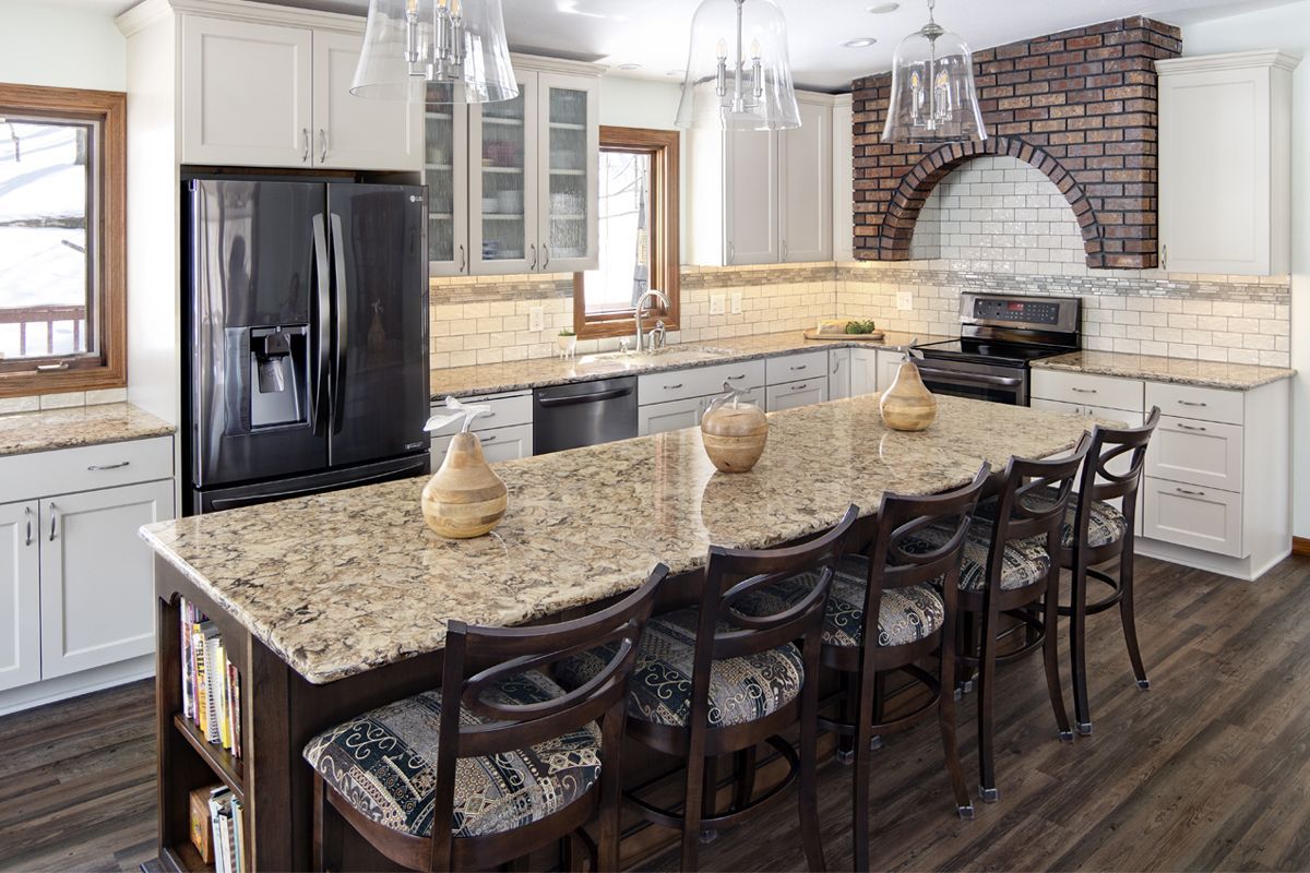 A kitchen with granite counter tops , stainless steel appliances , white cabinets and a large island.