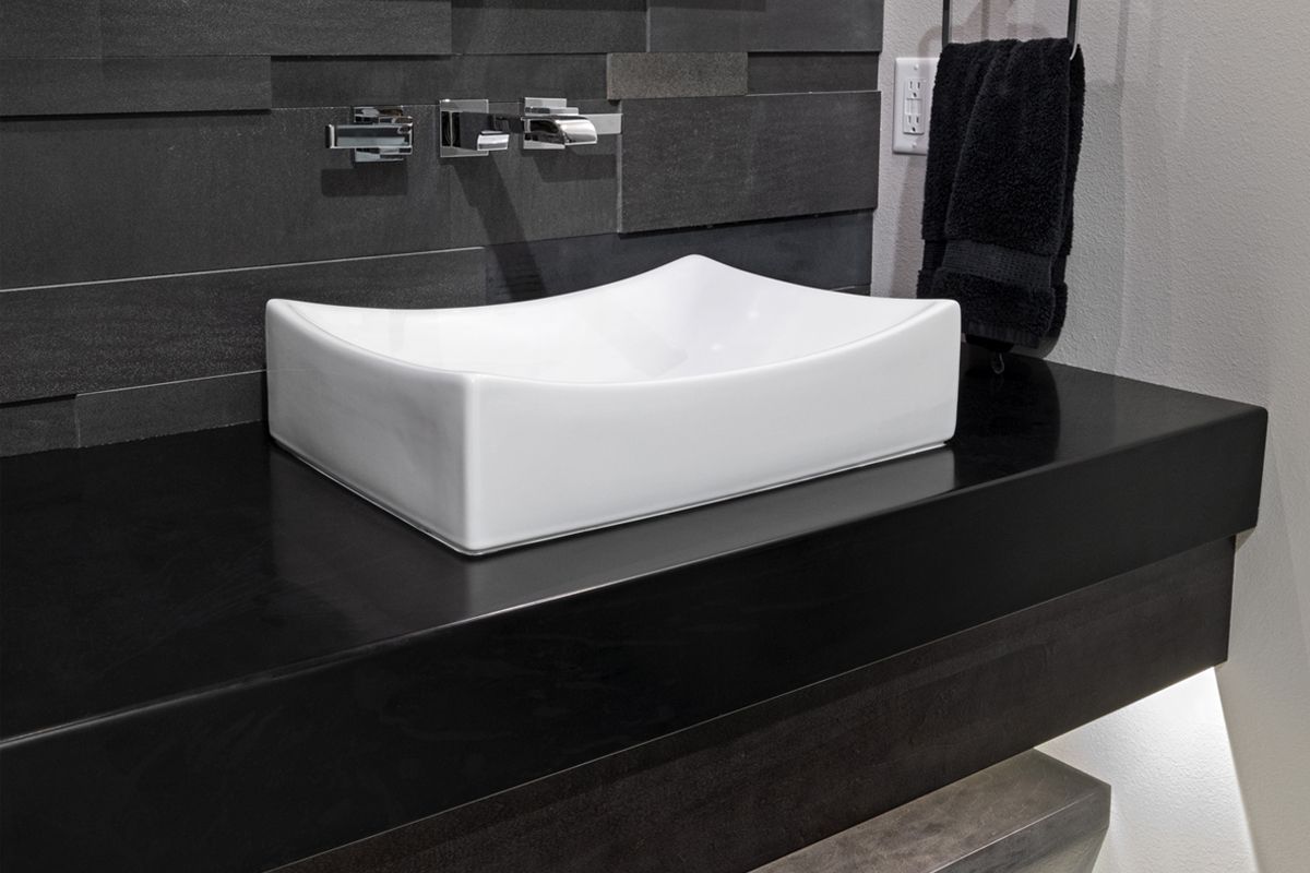 A white sink is sitting on a black counter in a bathroom.