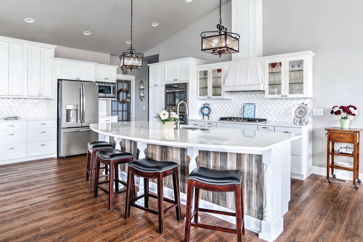A kitchen with white cabinets , stainless steel appliances , a large island and stools.