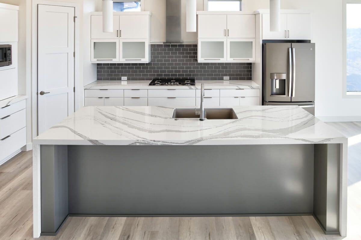 A kitchen with white cabinets , a stainless steel refrigerator , a sink , and a large island.