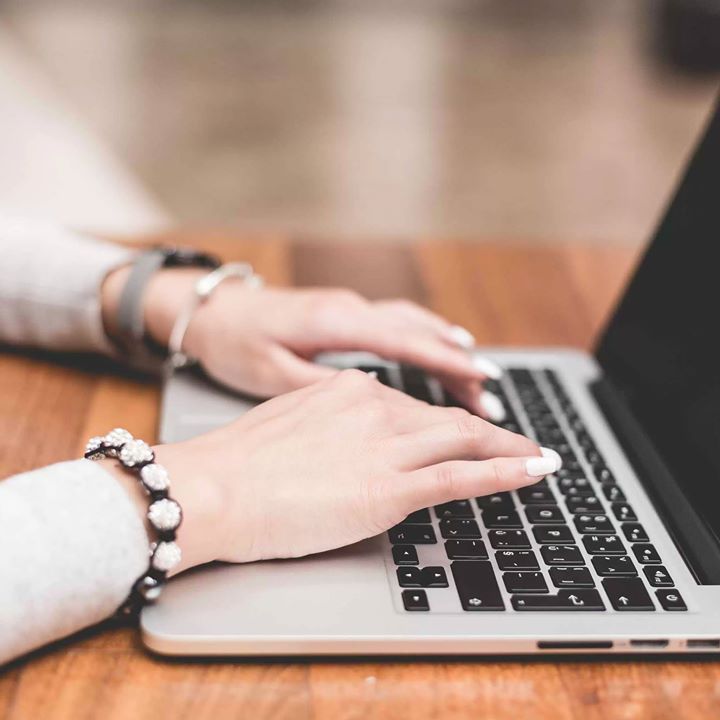 A woman wearing a bracelet is typing on a laptop