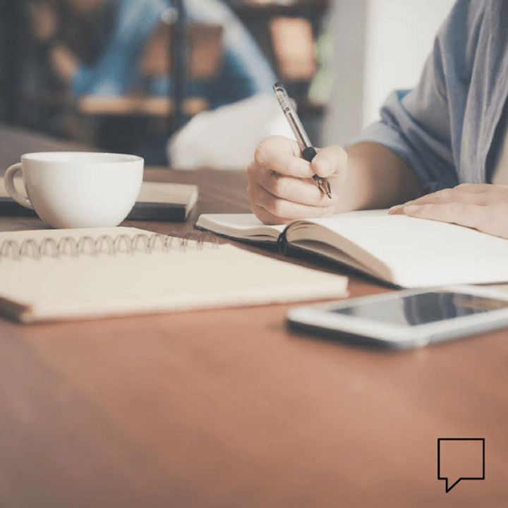 A person is sitting at a table writing in a notebook.