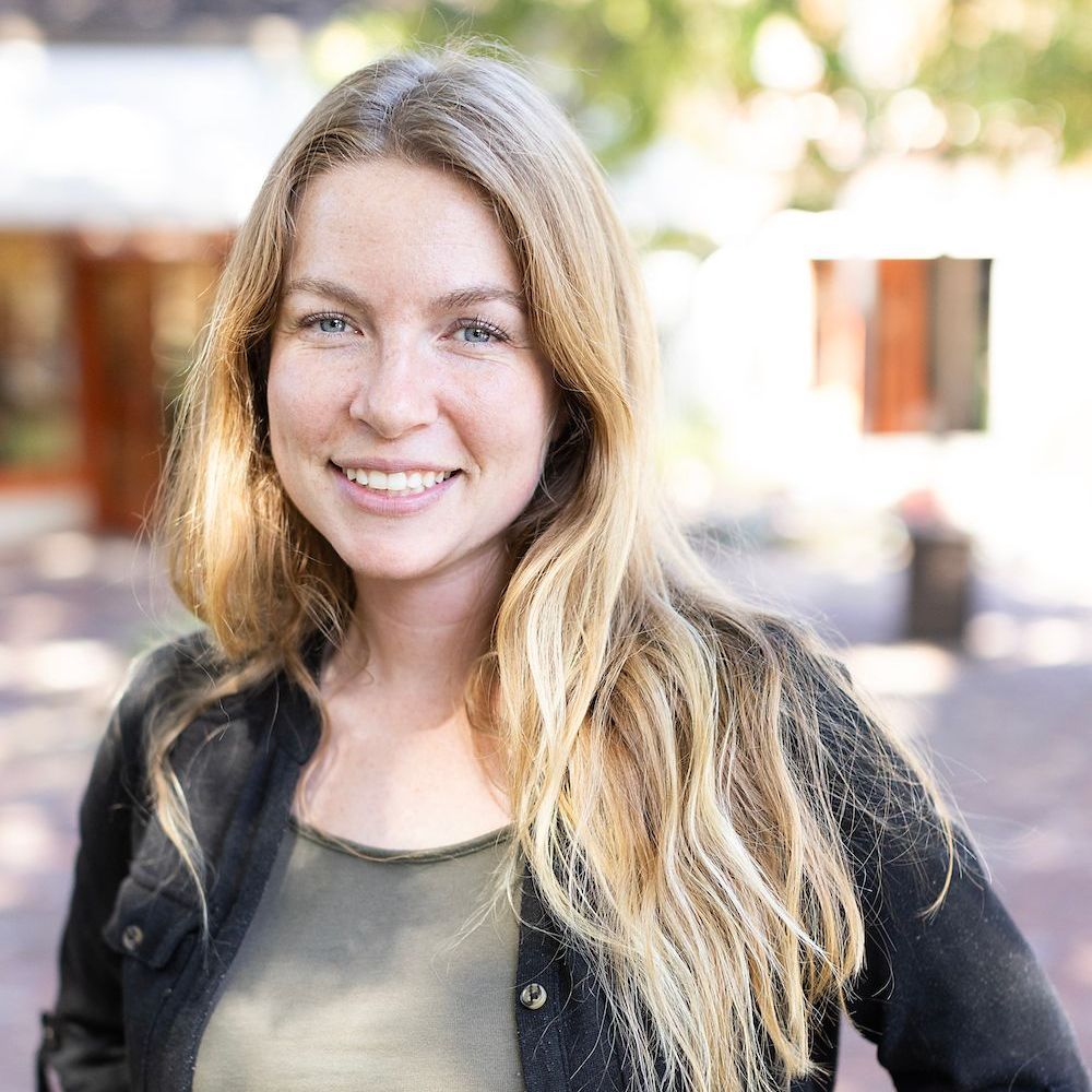 A woman with long blonde hair is smiling for the camera while wearing a black jacket.
